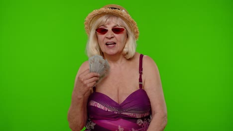 abuela madura viajero regocijándose de ganar la lotería, agitando un montón de dinero dólares en efectivo, sonriendo