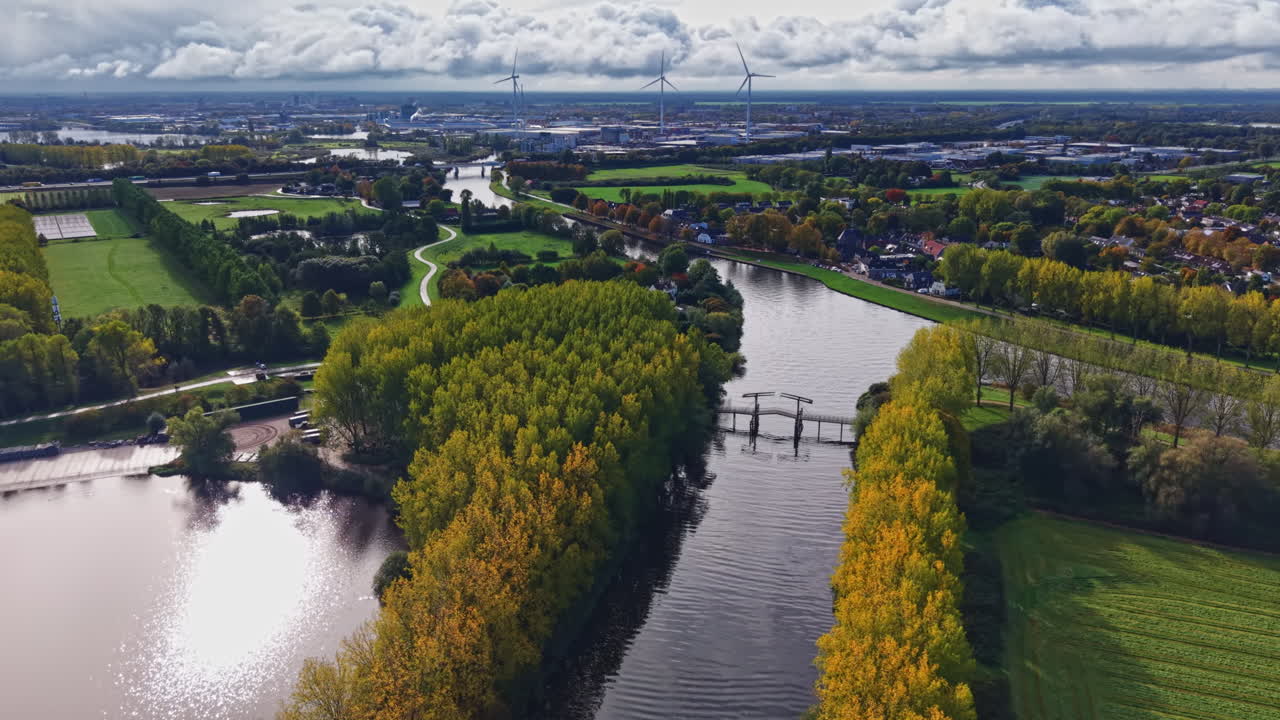 Fiume maestoso che si snoda attraverso lussureggianti paesaggi verdi sotto un cielo vibrante pieno di nuvole e luce solare vicino a una città moderna in autunno.