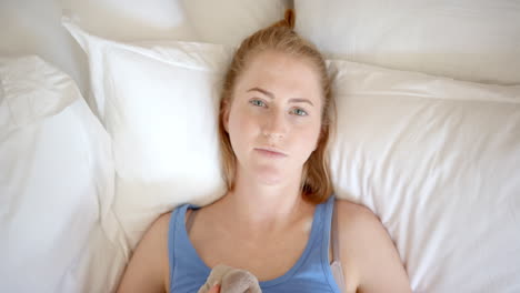 resting in bed, woman lying down and looking at camera, holding blanket