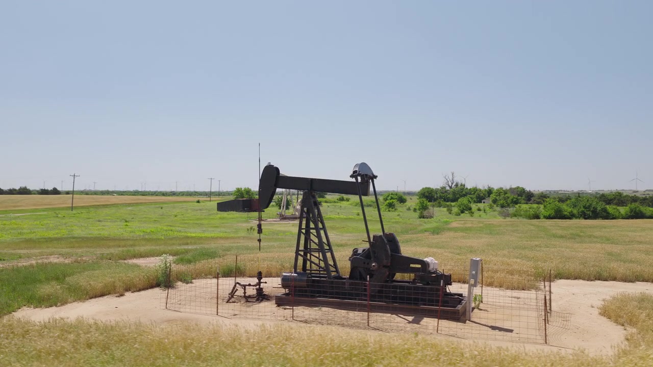 Drone 4K of a wheat field with two oil pump jacks and wind turbines in the background.