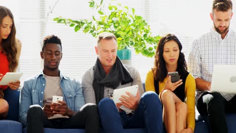 business colleagues using electronic devices while sitting on sofa