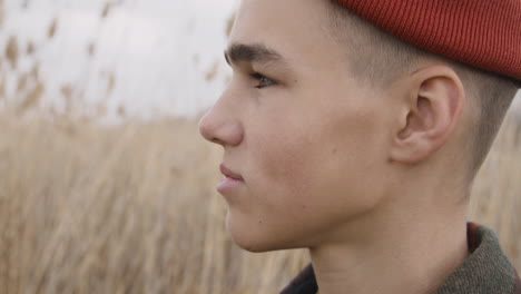 close up view of a teenage boy with orange beanie and plaid coat looking at side in a wheat field