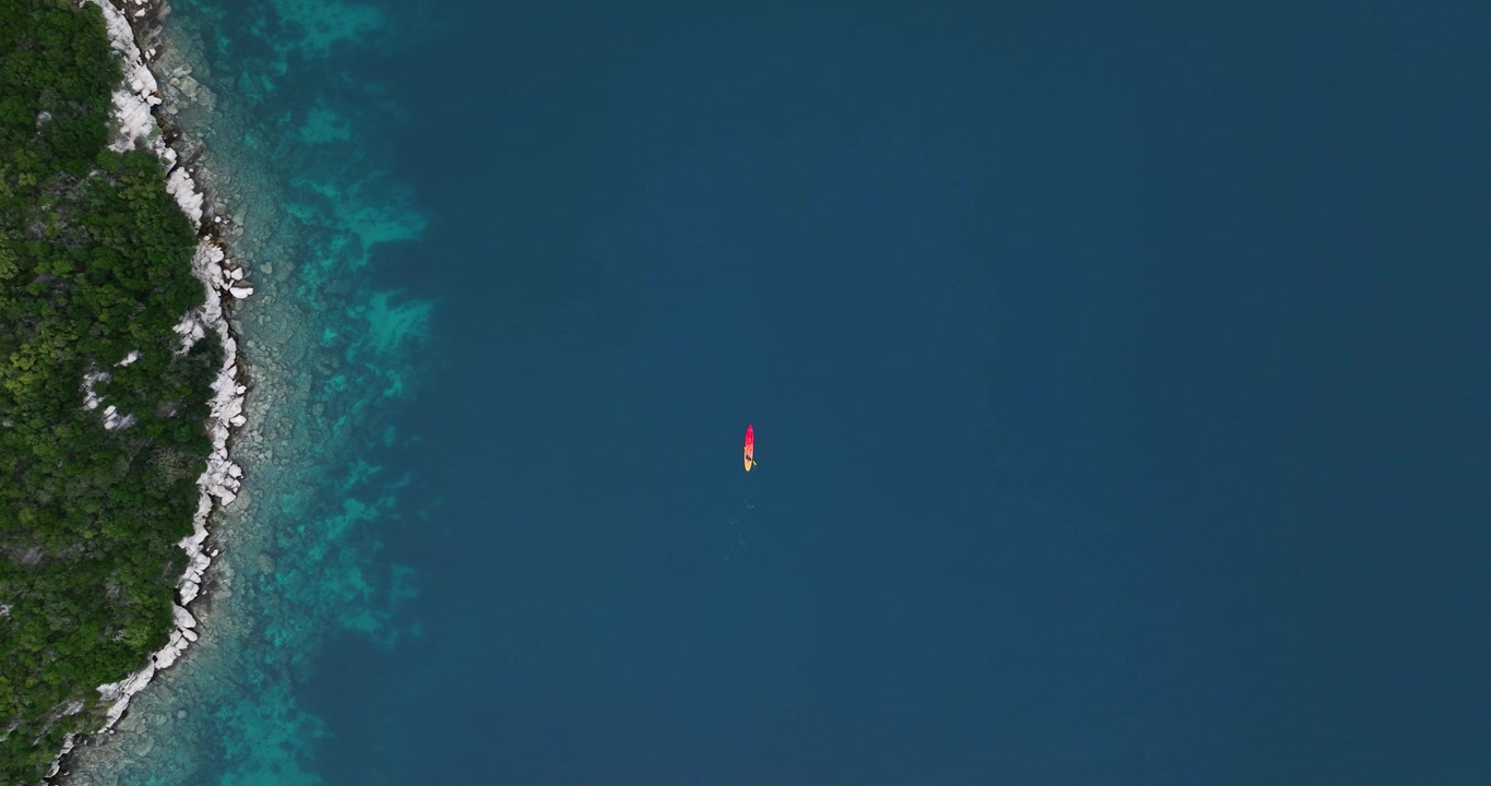 Un kayak solitario galleggia su acque blu profonde vicino alla costa rocciosa e verde di Mljet, evocando serenità.
