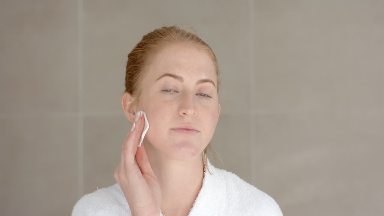 Applying skincare, woman cleansing face with cotton pad at home