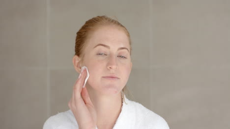 applying skincare, woman cleansing face with cotton pad at home