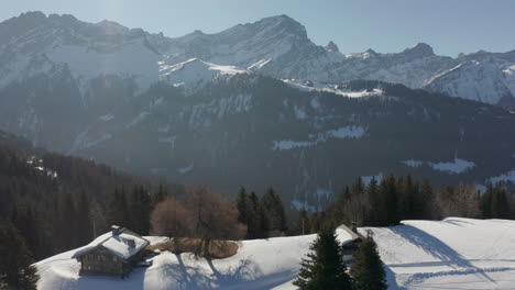 Aerial-view-of-beautiful-valley,-drone-pulling-back-and-revealing-small-cabins-in-snow-covered-landscape