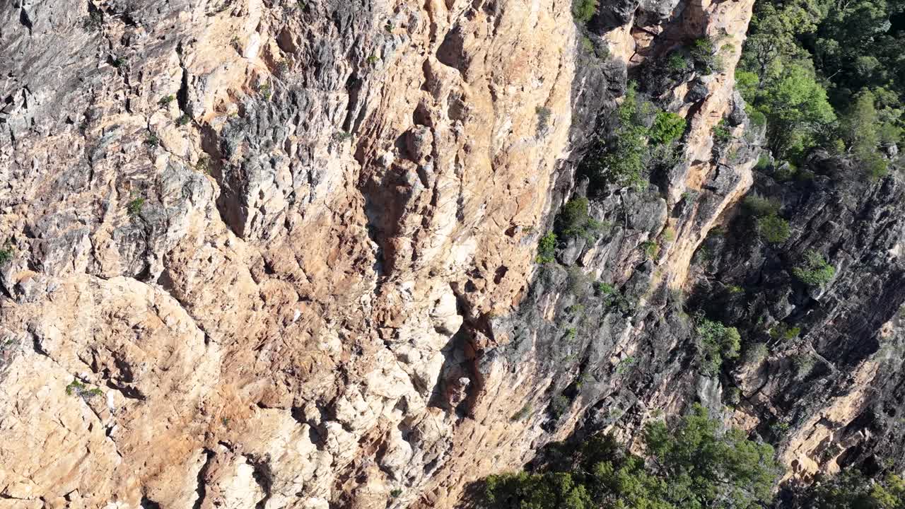 Dynamic aerial footage of Nimbin Rocks, showcasing rugged cliffs and lush greenery under bright daylight