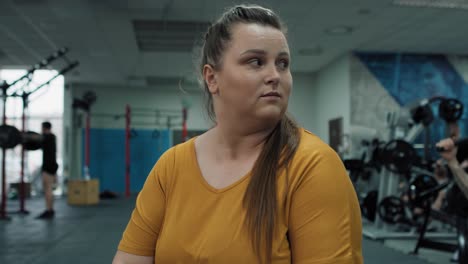 una mujer caucásica con sobrepeso se siente incómoda en el gimnasio.