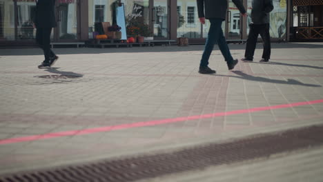 people walking across tiled pavement in an urban setting with shadows cast on the ground and storefronts visible in the background