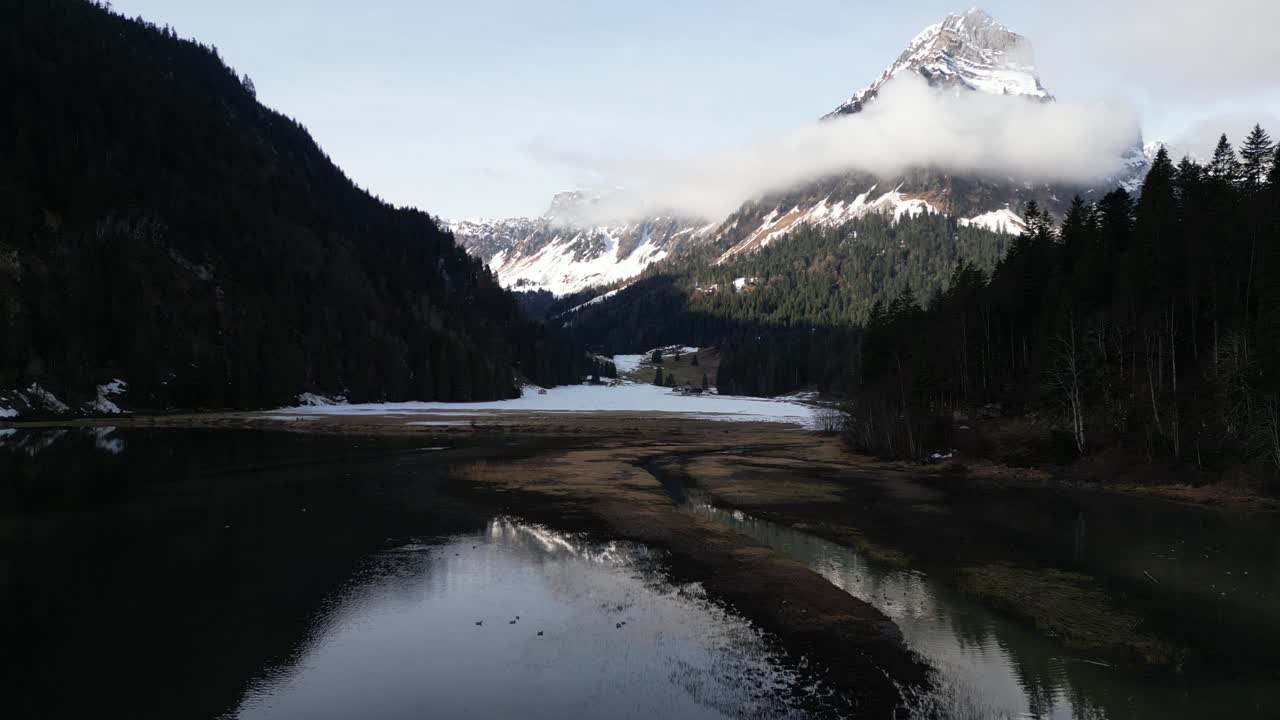 el dolly aéreo por encima de los niveles bajos de agua refleja las montañas cubiertas de nieve y nubes