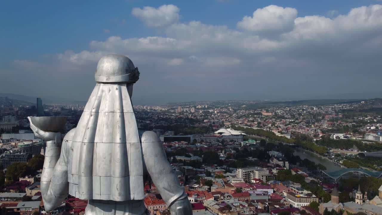 Tall metallic monument overlooking Tbilisi city skyline with mountains in background