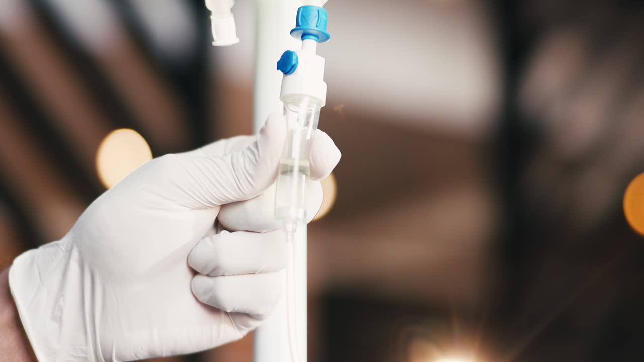 Mano guantata che regola una flebo endovenosa in un ambiente medico.