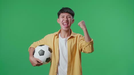 asian boy with a ball screaming goal celebrating for the winner team while cheering soccer on green screen background