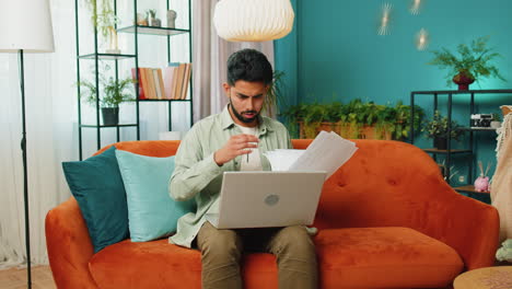 Stressed-Indian-man-looking-at-unpaid-bank-debt-loan,-doing-paperwork,-planning-budget,-throws-bills