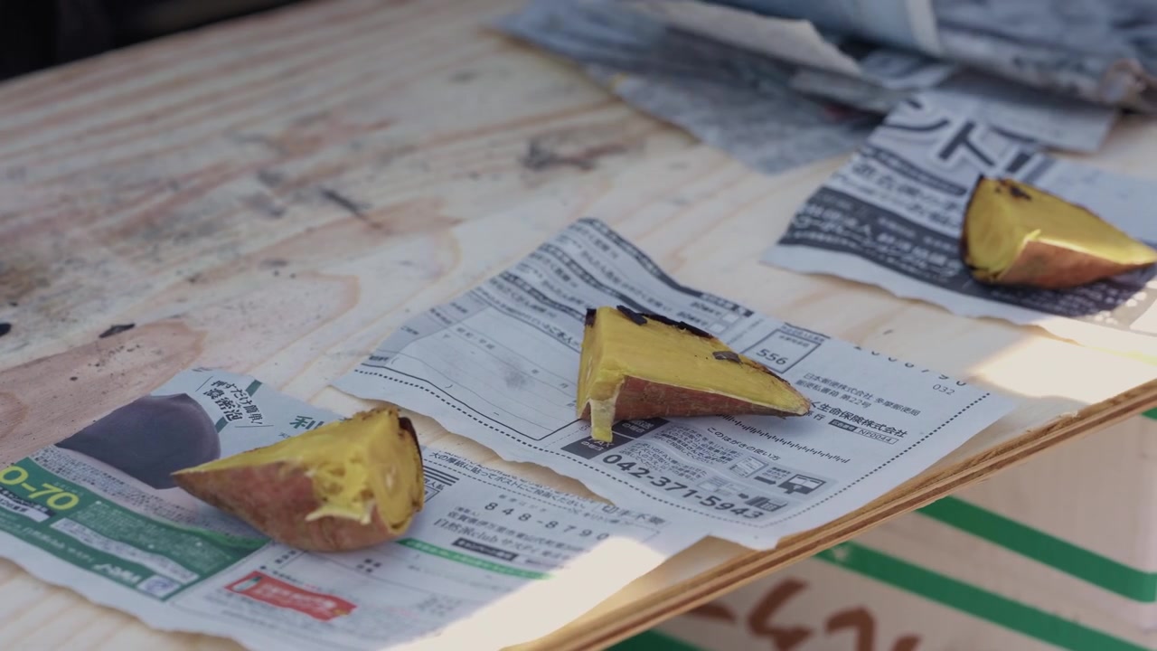 Fette di patata dolce giapponese arrosto dorate su un giornale con una mano che afferra un pezzo in Giappone
