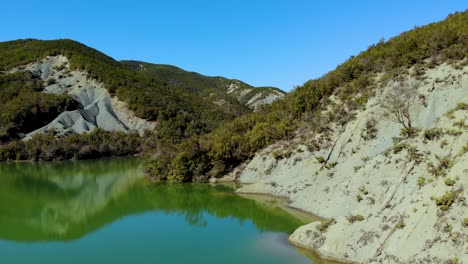 Friedlicher-Bergsee-Mit-Ruhigem,-Klarem-Wasser,-Das-Schöne-Wilde-Naturhänge-Mit-Grüner-Vegetation-Unter-Strahlend-Blauem-Himmel-Widerspiegelt