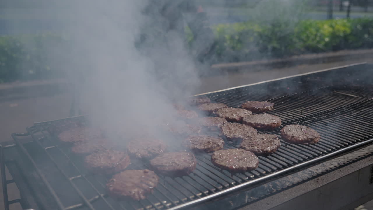 Hamburger su barbecue a carbone untuoso e fumoso in un pomeriggio estivo su griglia commerciale al rallentatore