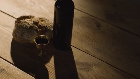 concepto religioso filmado con pan de cáliz y vino en una mesa de madera con un charco de luz