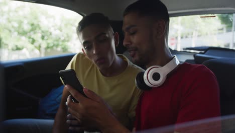 two happy mixed race friends holding coffee and using smartphone in cab