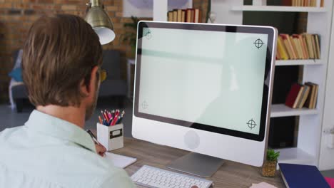 Caucasian-male-teacher-taking-notes-while-having-a-videocall-on-computer-in-the-classroom-at-school