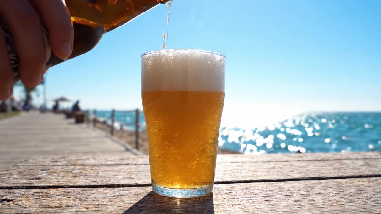 Un momento rinfrescante in riva al mare: versare una bevanda fredda in un bicchiere sotto il sole splendente con una vista mozzafiato sul mare.
