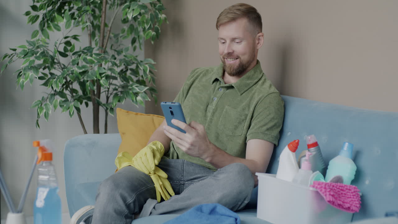 Man Cleaning and Using Smartphone at Home