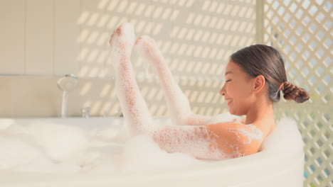 happy asian woman takes a bath and plays with soap in bathtub