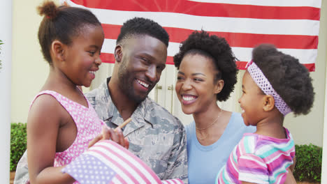 African-american-male-soldier-embracing-his-smiling-family-over-american-flag