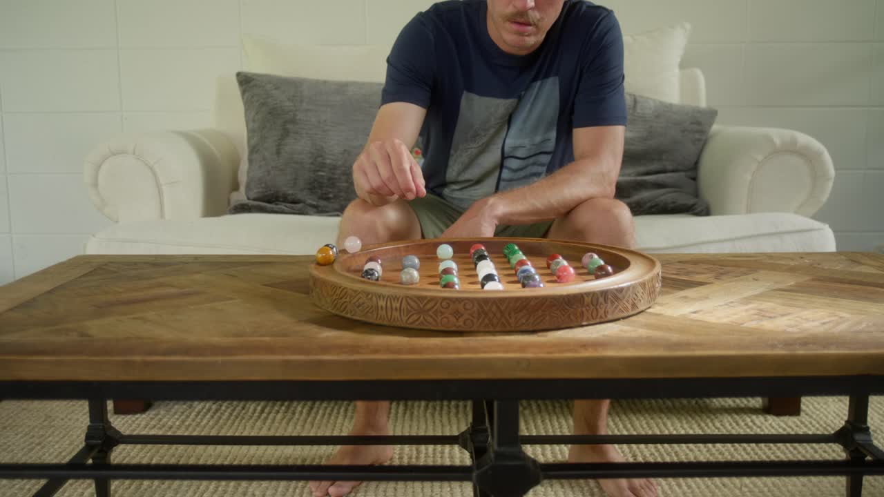Um homem relaxa em uma casa de luxo enquanto joga um jogo de mesa de Paciência de madeira ornamentado em uma elegante mesa de centro de madeira.