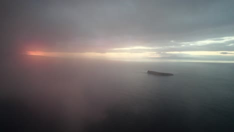 cinematic slow aerial shot through clouds over the pacific ocean with molokini crater and the sacred island of kaho'olawe in the distance during amazing sunset on maui, hawai'i