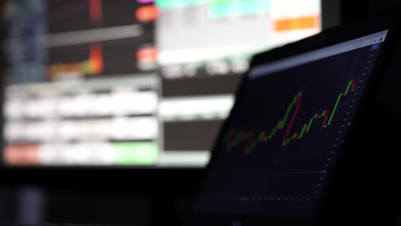 gráficos bursátiles moviéndose en las pantallas de dos computadoras, 4k