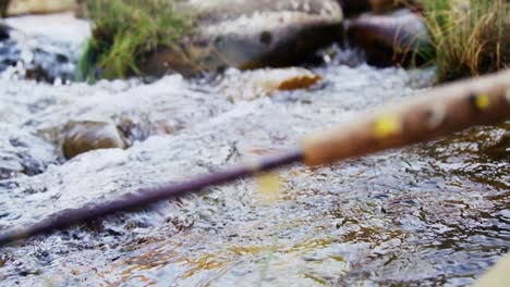 caña de pesca con mosca, carrete y gancho en roca