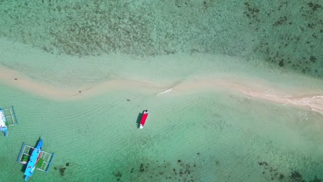 rising aerial over thin winding sandbank beach and tour boats in tropical clear lagoon, snake island in el nido