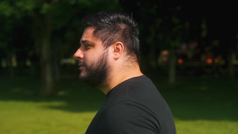 young man walking by outdoors at a park with trees grass and lake view