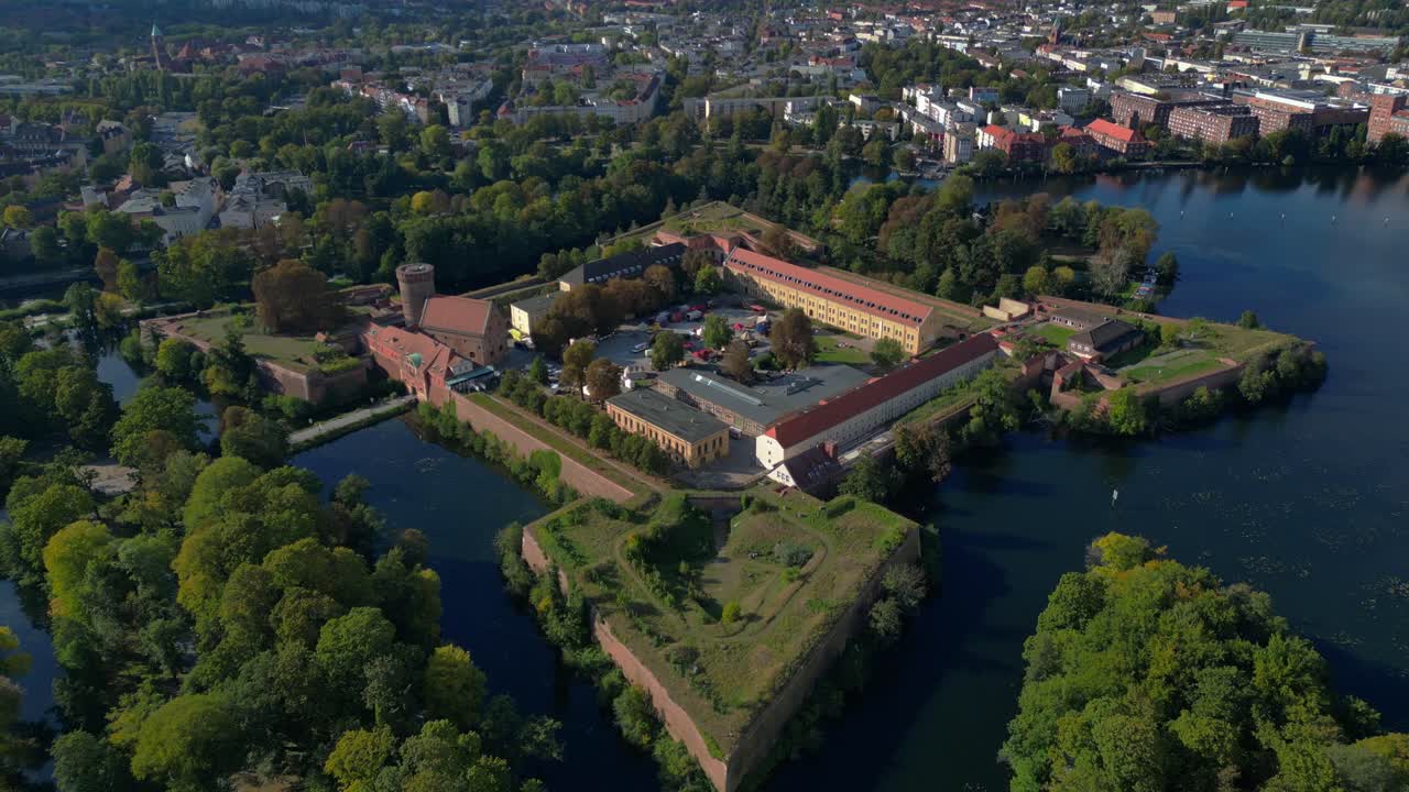 Spandau Citadel, an imposing Renaissance fortress surrounded by water, stands under a clear sky. Unique aerial view flight ascending drone