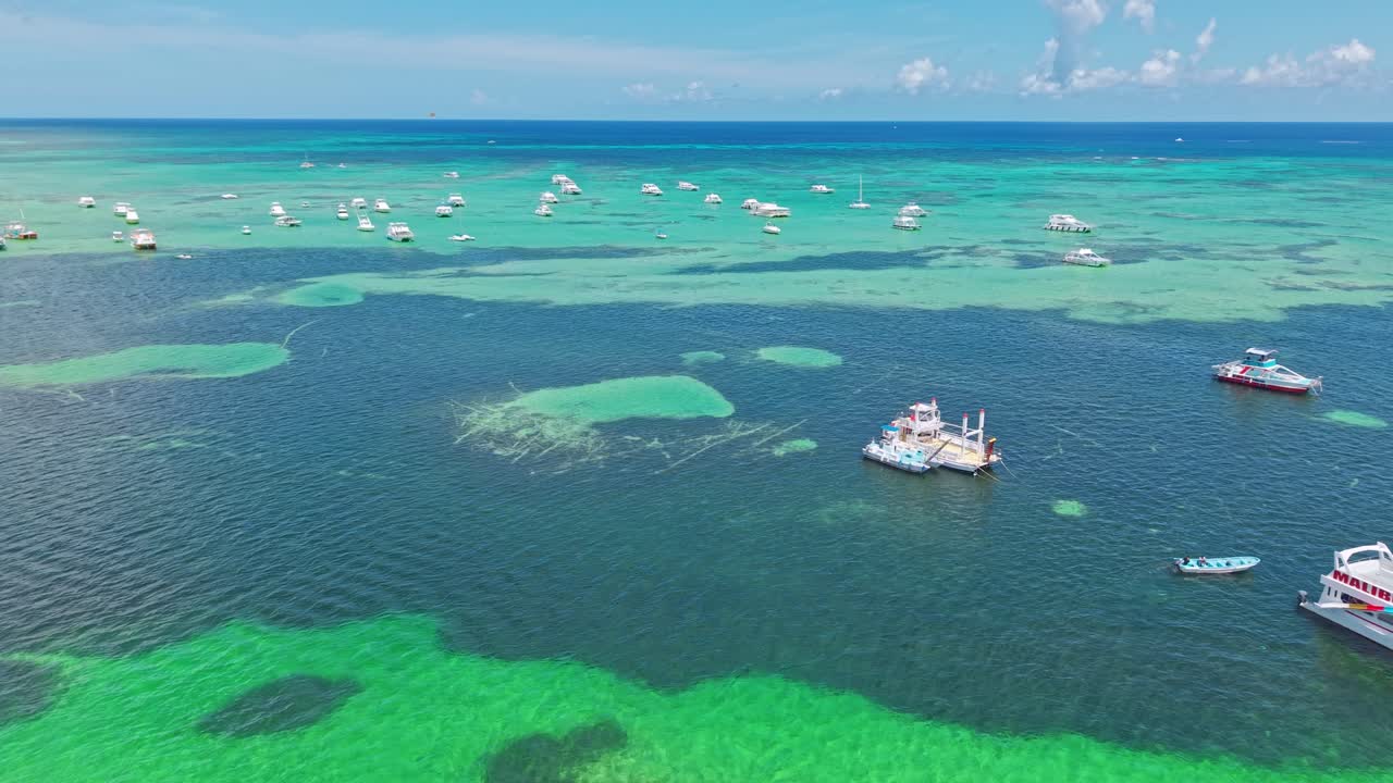 Yachts and boats at shoreline of Punta Cana beach in Dominican Republic. Sunny summer day with crystal clear Caribbean Sea and coral reef. Drone flyover shot