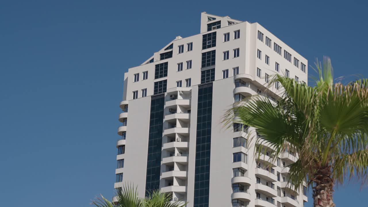 Wide shot of palm tree, blue sky and white building during the day in Durres, Albania