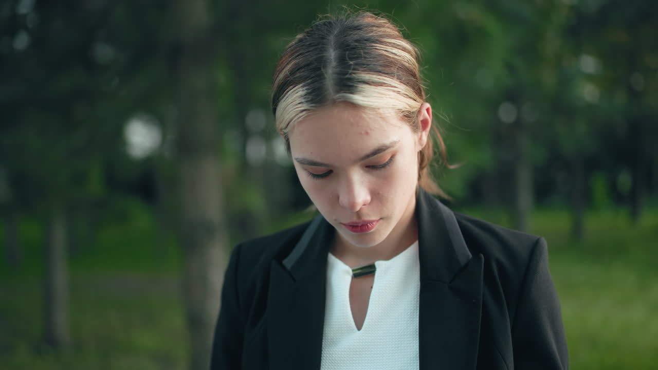 Professional lady focuses deeply while drinking coffee outdoors, surrounded by trees as sunlight filters through leaves, creating natural ambiance and peaceful work atmosphere in green park setting