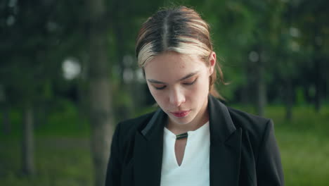professional lady focuses deeply while drinking coffee outdoors, surrounded by trees as sunlight filters through leaves, creating natural ambiance and peaceful work atmosphere in green park setting