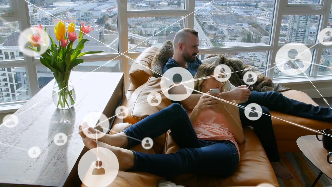 Ikony profilů propojené čarami nad bělošským párem relaxujícím na gauči a používajícím chytré telefony.