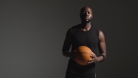 Foto-De-Estudio-De-Un-Jugador-De-Baloncesto-Masculino-Caminando-Hacia-La-Cámara-Sosteniendo-Bal