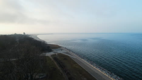 aerial flying over the coastline of the baltic sea at sunset on foggy day in westerplatte, poland