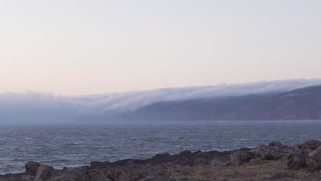 clouds rolling over the mountains into the sea at guincho beach in portugal
