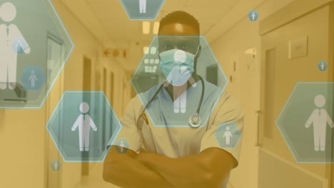 Animation-of-icon-in-hexagons-over-african-american-male-doctor-standing-arms-crossed-in-hospital