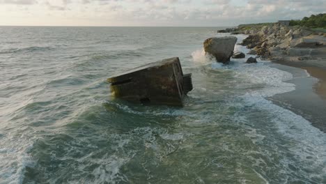 beautiful aerial establishing view of karosta concrete coast fortification ruins, sunny summer evening, golden hour light, stormy waves at baltic sea, slow motion drone shot moving forward