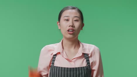 nahaufnahme einer wütenden asiatischen hausfrau mit einer schürze, die auf die kamera zeigt und schreit, während sie im grünen bildschirmstudio steht