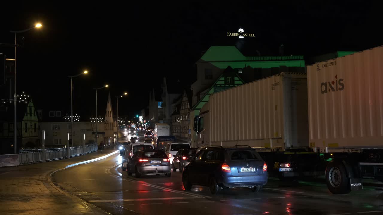 Traffic jam at the entrance of the german city Stein, with many cars and trucks moving at a slow pace. Its a night scene with many red brake lights.