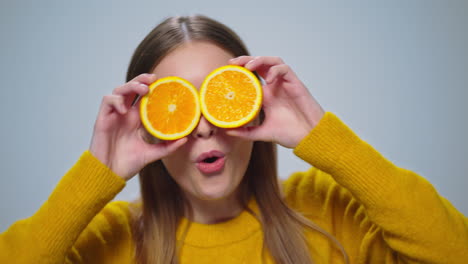 retrato de una mujer alegre divirtiéndose con dos rebanadas de naranja en el estudio.