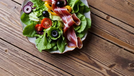 fresh salad with prosciutto and vegetables on a wooden table