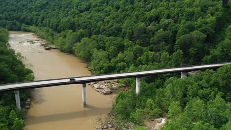 dark van passing bridge above muddy river, aerial view, lush green forest and roadway in west virginia usa